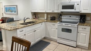 A kitchen with white cabinets, a granite countertop, a built-in microwave, a stove, and a sink. - Beach views, poolside, new kitchen,  2 BR beach condo, KING bed ~ FN 304 (St Pete Beach)