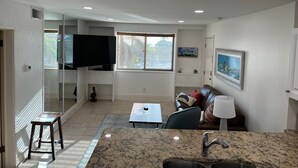 A modern living room with a flat-screen TV, a sofa, a coffee table, and a kitchen area with granite countertops and a sink. - Beach views, poolside, new kitchen,  2 BR beach condo, KING bed ~ FN 304 (St Pete Beach)
