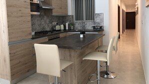 A modern kitchen with wooden cabinetry, a central island with bar stools, a stainless steel range hood, and a patterned backsplash. - Azure Cottage: Beautiful, modern 3 bedroom apartment with communal swimming pool (Marsalforn)