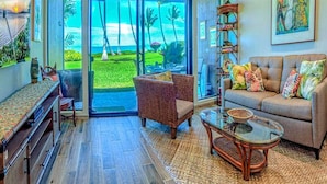 Amplia sala de estar con un gran ventanal que da a un jardín tropical, muebles de mimbre y un sofá con cojines de colores.