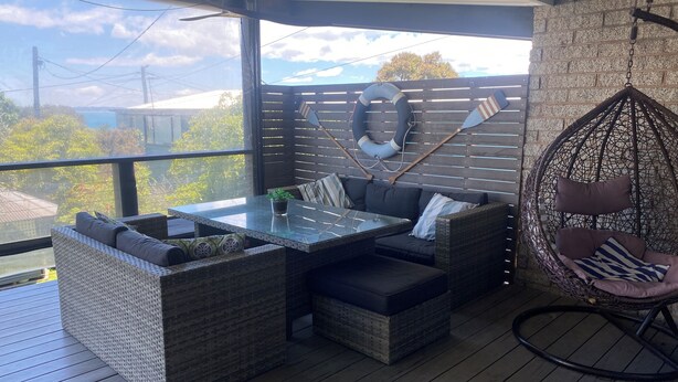 Un espace extérieur aménagé avec des meubles en osier, une table à plateau en verre et un fauteuil suspendu.
