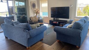 Un salon moderne avec deux canapés bleus, une table basse en verre et un téléviseur à écran plat.
