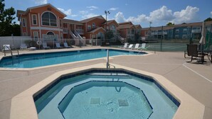 Un área de piscina con sillas de descanso y un jacuzzi, rodeada de edificios de estilo arquitectónico clásico.