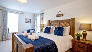 A bedroom with a wooden headboard, a large bed with a navy blue bedspread, two bedside lamps, and a small bedside table with a lamp. - Harbour View - A6 Masts (Torquay)