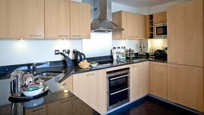 A modern kitchen with wooden cabinets, stainless steel appliances, and a black countertop. - Harbour View - A6 Masts (Torquay)