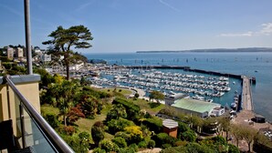 A marina with numerous boats docked, surrounded by lush greenery and a clear blue sky. - Harbour View - A6 Masts (Torquay)