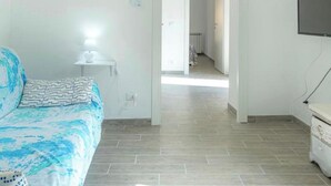 Ett sovrum med en säng, ett sängbord med en lampa, en tv som är monterad på väggen och en hall som leder till ett annat rum.