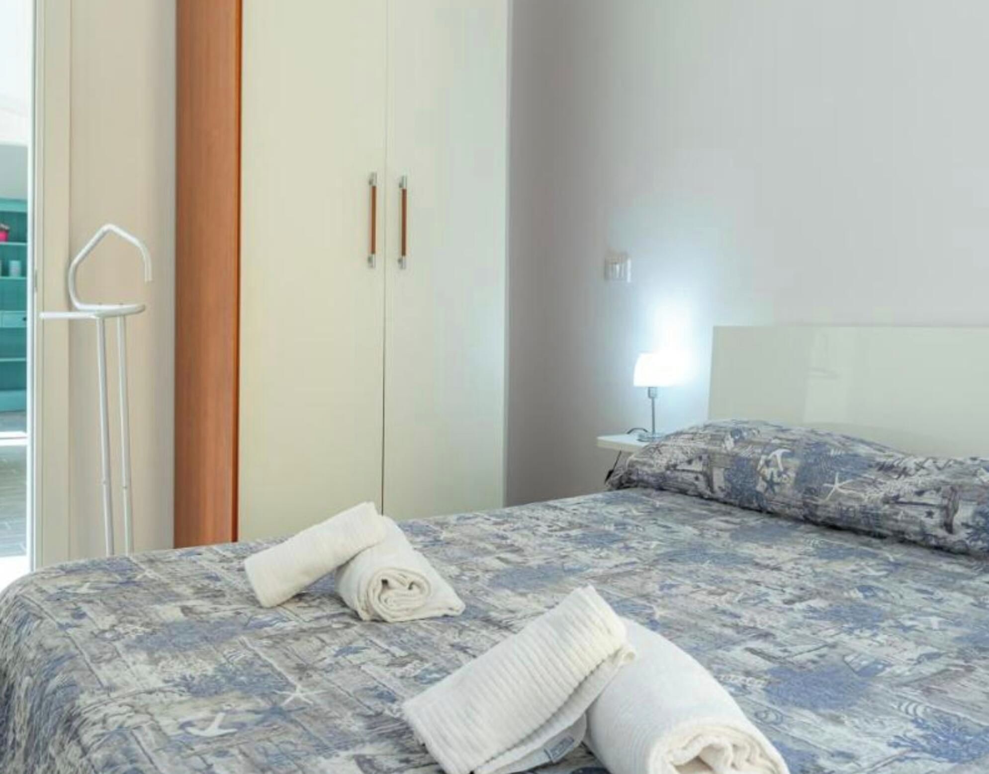 A hotel room with a bed, a nightstand, a lamp, and a wardrobe.