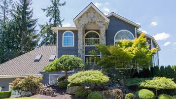A two-story house with a stone facade, a gabled roof, and a large arched window.
