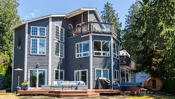A multi-story house with a deck, large windows, and a covered outdoor seating area.