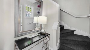A hallway with a mirror, a black console table with a lamp, and a staircase. - A Pleasant Stay at The Truman Annex in Key West (Key West)