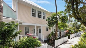 A two-story house with a porch, surrounded by lush greenery and a white picket fence. - A Pleasant Stay at The Truman Annex in Key West (Key West)