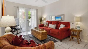 A living room with a red sofa, a wooden coffee table, a patterned rug, and a ceiling fan. - A Pleasant Stay at The Truman Annex in Key West (Key West)