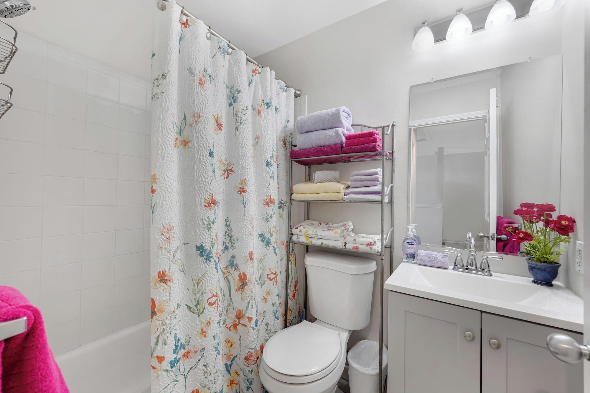 Une salle de bain avec un rideau de douche, des toilettes, un lavabo avec un miroir et une étagère avec des serviettes.