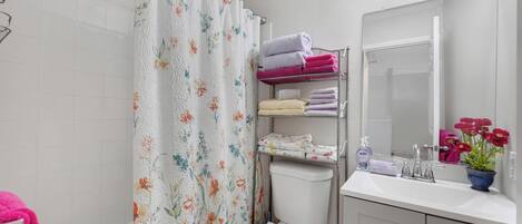 Une salle de bain avec un rideau de douche, des toilettes, un lavabo avec un miroir et une étagère avec des serviettes.