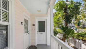 A porch with a white door marked "102 11-", a doormat, and a white railing. - A Pleasant Stay at The Truman Annex in Key West (Key West)
