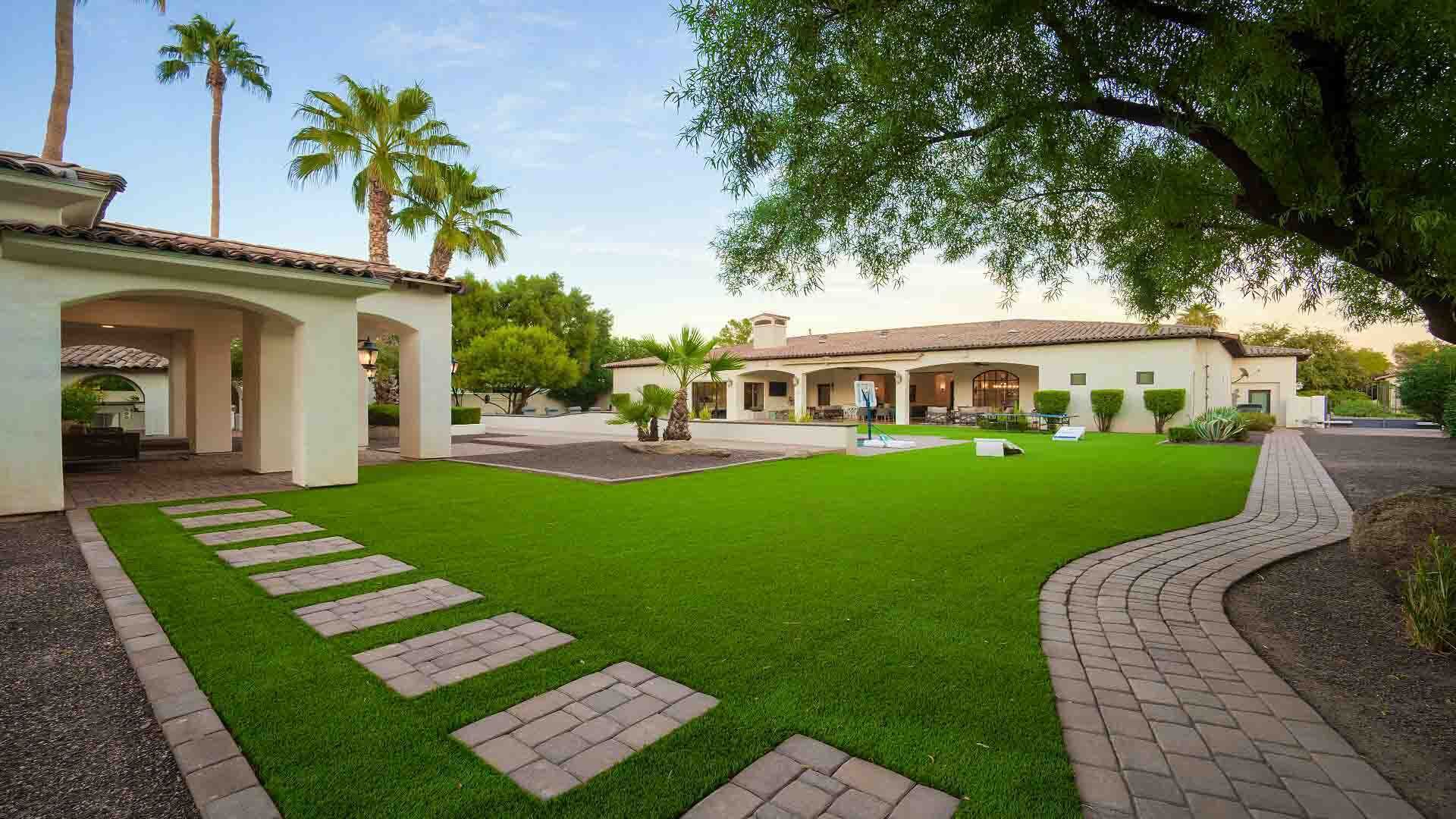 A well-maintained courtyard with a lawn, paved walkways, and a building with a tiled roof and arches.