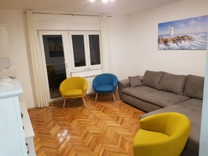 A living room with a wooden herringbone floor, a grey sofa, and two armchairs, one yellow and one blue.