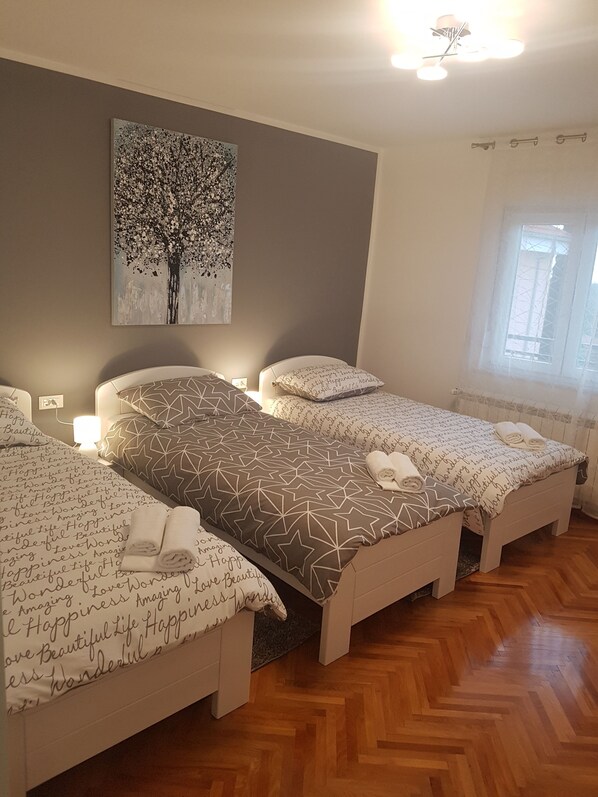 A hotel room with three beds, a large tree painting on the wall, and a window with curtains.