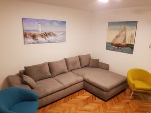 A living room with a sectional sofa, a blue armchair, a yellow armchair, and two paintings on the wall.