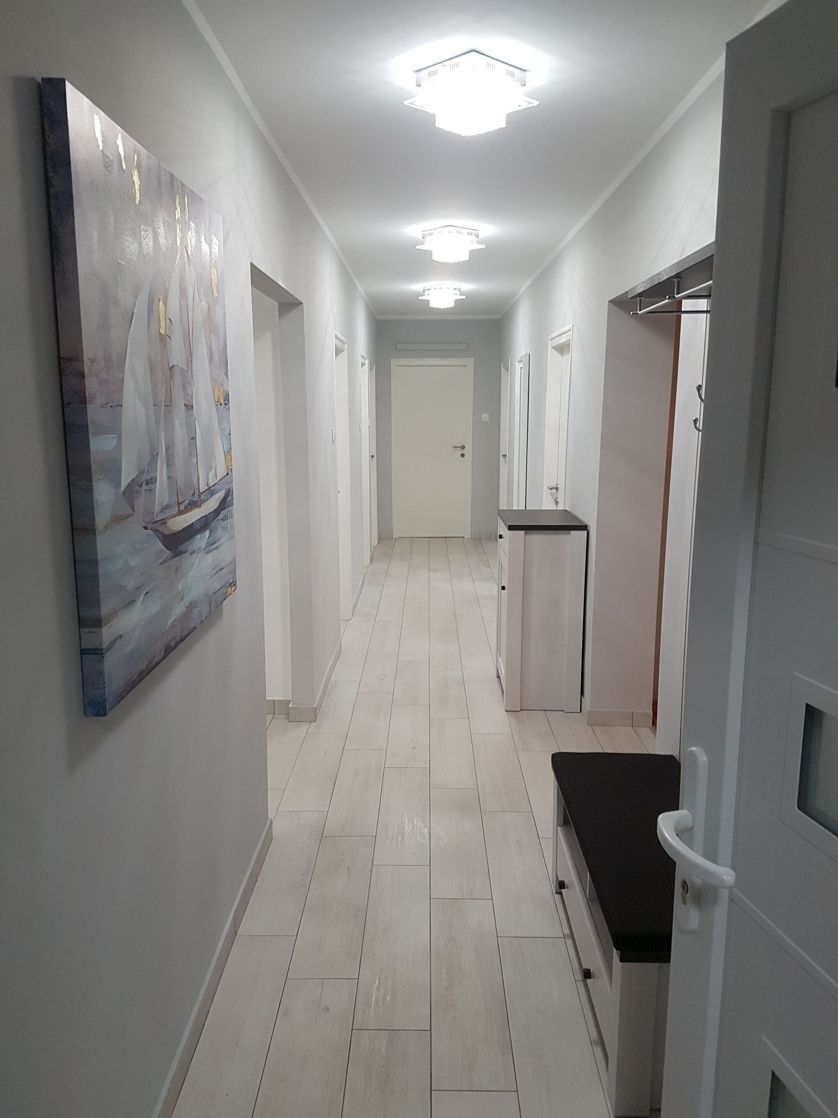 A hallway with a painting of a sailboat on the left, a bench with a black seat, and a door on the right.
