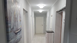 En hall med en målning av en segelbåt på vänster sida, en bänk med en svart sits och en dörr på höger sida.