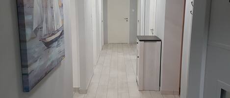 A hallway with a painting of a sailboat on the left, a bench with a black seat, and a door on the right.