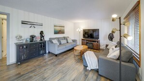 A modern living room with a grey sofa, a coffee table, and a TV. There is a cabinet with glass doors and a fan. - Cozy Worley Cabin w/ Lake Access + Gas Grill! (Worley)