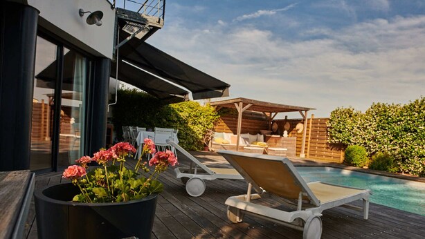 A wooden deck with a pool, lounge chairs, and a planter with pink flowers. - Bruges, Near Bordeaux: Charming, Air-Conditioned House with a Pool and Garden (Bruges proche Bordeaux)