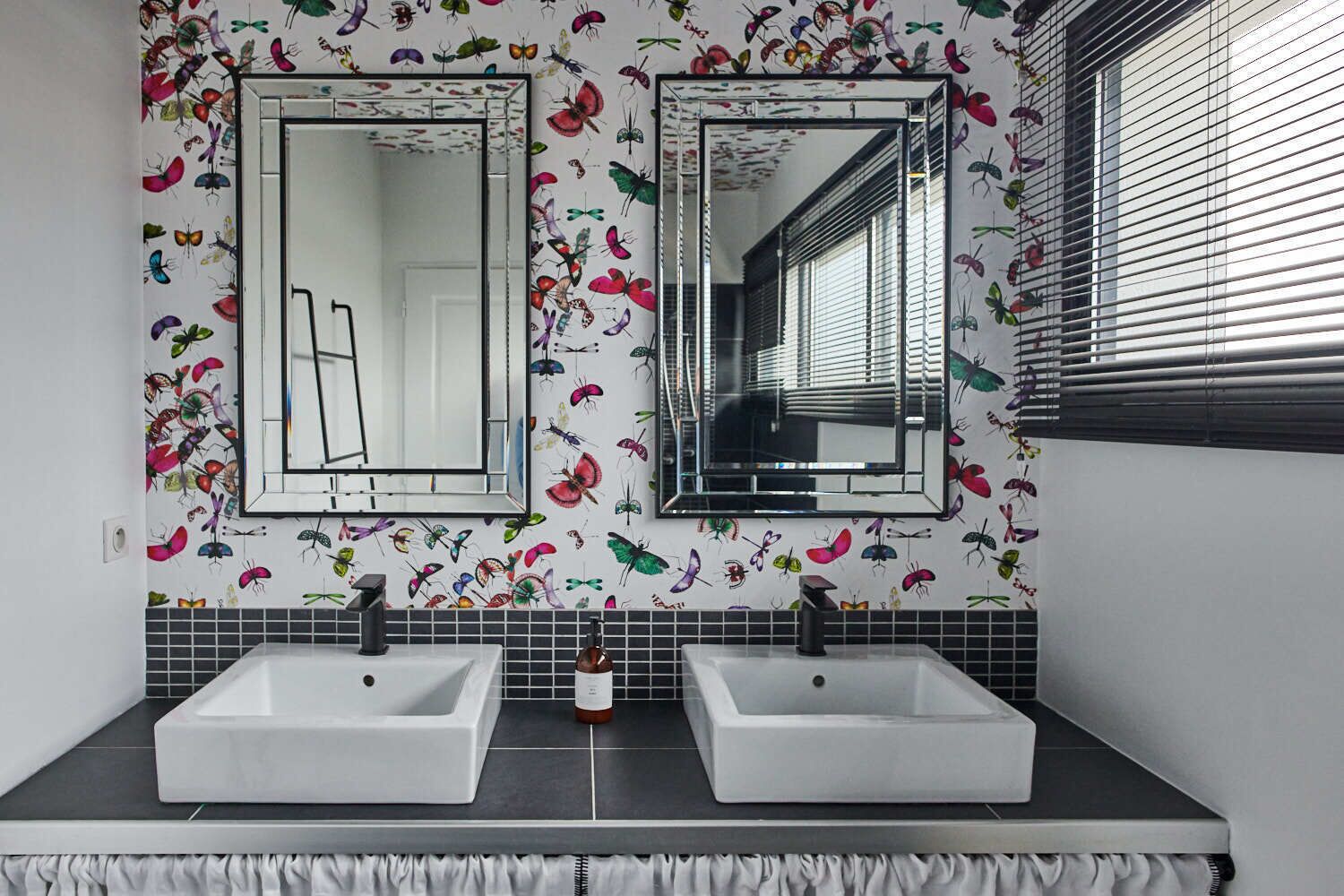 A bathroom with two sinks, a mirror, and a window with blinds.