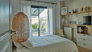 A bedroom with a bed, a hanging light fixture, a window with curtains, a radiator, and a TV on a shelf. - Bruges, Near Bordeaux: Charming, Air-Conditioned House with a Pool and Garden (Bruges proche Bordeaux)