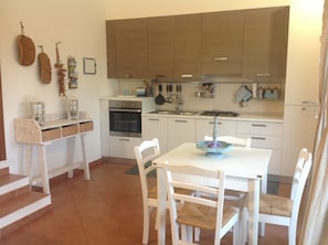 Une cuisine avec des meubles blancs, une cuisinière, un four et une table à manger avec des chaises.