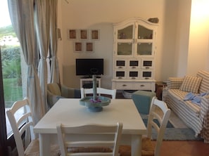 Un coin repas avec une table et des chaises, un téléviseur, un meuble avec des portes en verre et un canapé.