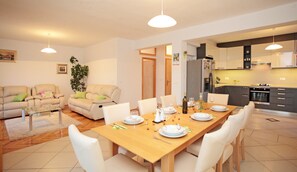 A modern living room with a dining area, featuring a wooden dining table set for four, white chairs, a beige sofa, and a small side table. - Magnificient panoramic view, wideview terrace, relaxing hot tube (Hrvatska, Vrboska)