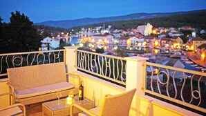 Un balcon agrémenté de meubles en osier, une table avec une bouteille et un verre, et une vue sur une ville au crépuscule.