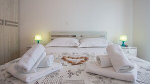 Un lit bien fait, avec des draps blancs, deux lampes de chevet et une composition en forme de cœur faite de coquillages disposée sur la couverture.