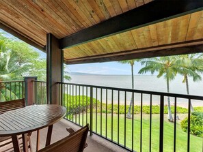 Een houten terras met een tafel en stoelen, met uitzicht op een strand met palmbomen en een zeezicht.
