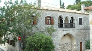 A stone building with a tiled roof, arched windows, and a balcony.