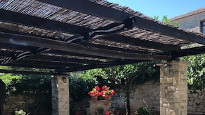 Un patio al aire libre con pilares de piedra, una pérgola y una mesa con sillas.