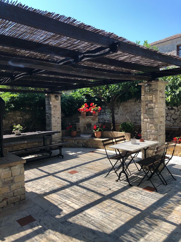 An outdoor patio with stone pillars, a pergola, and a table with chairs.