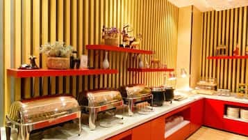 Disposição de buffet com várias estações de serviço, decoração em vermelho e branco, e padrões de parede listrados.
