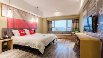 Quarto de hotel moderno com uma cama grande, uma escrivaninha, uma televisão e vista para o mar.