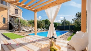 Un cadre agréable au bord de la piscine, avec une pergola, une bouteille de champagne et une assiette de fruits sur une table.