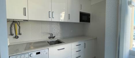 Uma cozinha compacta com armários brancos, micro-ondas embutido, máquina de lavar e pia.