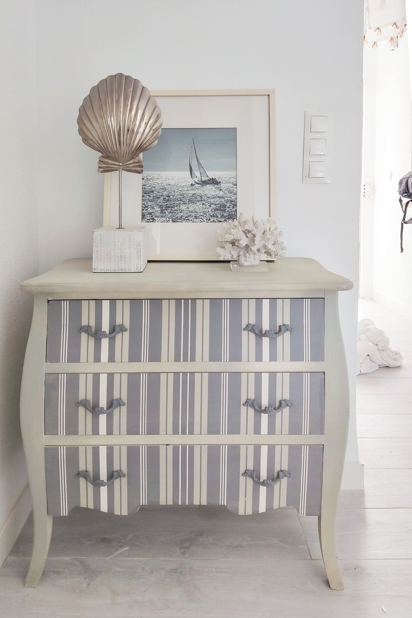 Une commode sur le thème de la côte, avec des tiroirs à rayures et un tableau encadré représentant un voilier.