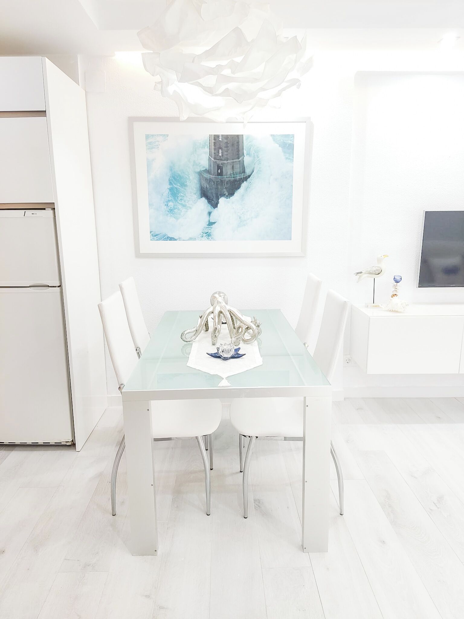A modern dining area with a glass-top table, white chairs, and a decorative sculpture.