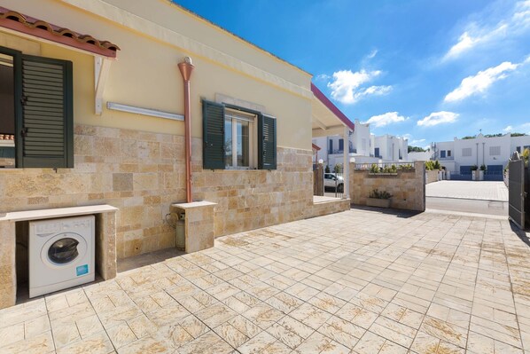 Un edificio residencial con un patio empedrado, lavadora y una ventana con contraventanas.