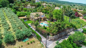 A large house with a swimming pool, surrounded by lush greenery and palm trees.
