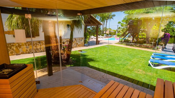 A covered patio with a wooden deck, a stone wall, and a view of a swimming pool and garden.