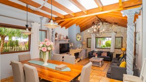 A spacious living area with a wooden dining table, comfortable seating, a stone fireplace, and a large window offering a view of greenery.